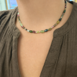 Close-up of a multicolored bead necklace resting on a person’s collarbone over a brown blouse.