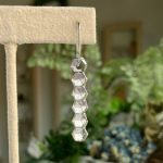 Silver earring made of stacked hexagonal beads hanging from a metal hook on a display stand, shown in a shop setting.