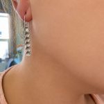 Close-up of a woman's ear with a silver hexagon drop earring featuring six connected hexagons.