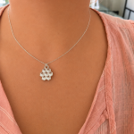 Silver honeycomb pendant necklace resting on a peach blouse.
