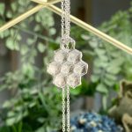 Silver honeycomb pendant necklace on a delicate chain, hanging against a blurred green background.