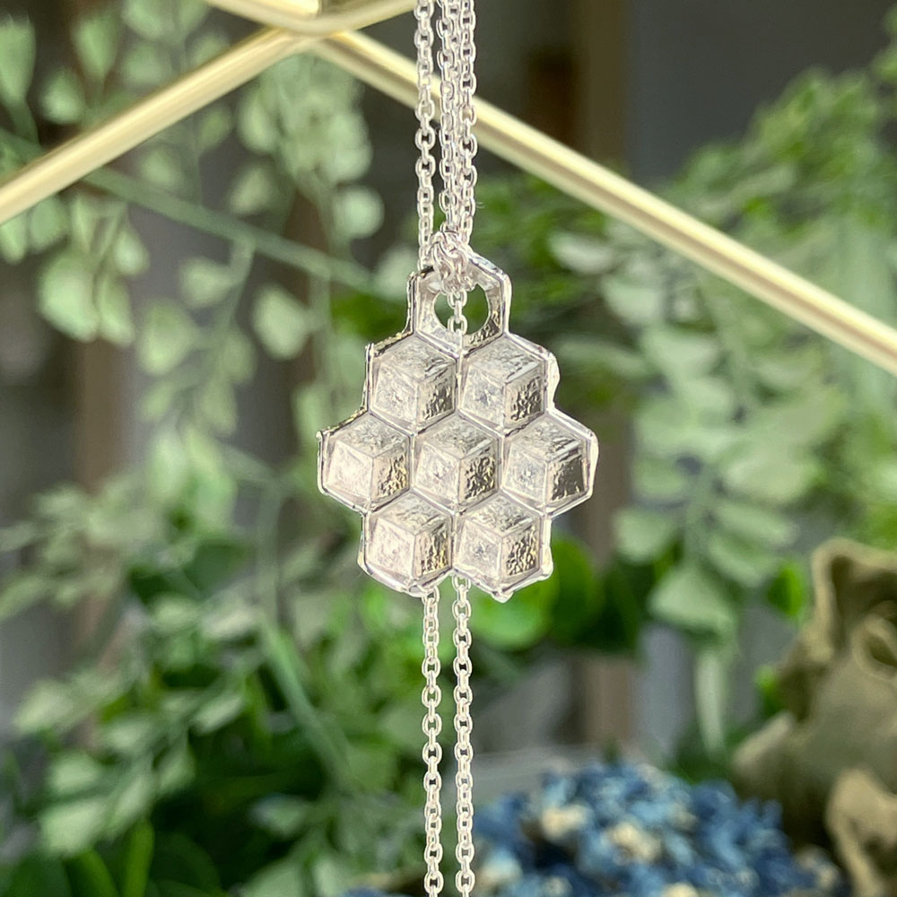 honeycomb silver pendantjpeg | Posy Fine Jewellery Toronto Silver honeycomb pendant necklace on a delicate chain, hanging against a blurred green background.