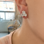 Close-up of a woman's ear wearing a three-hexagon clear jewelry earring in a honeycomb design on the earlobe