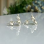 Pair of silver cufflinks with textured, faceted fronts resting on a reflective white surface, showing their reflections.