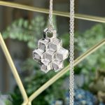 Silver pendant shaped like a honeycomb made of interlocking cubes, hanging from a delicate chain.