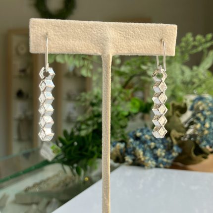 Silver dangle earrings with stacked hexagonal beads on a display stand, close-up view in a jewelry shop setting