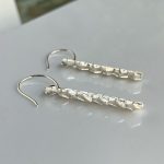 Silver drop earrings with twisted textured bars and curved hooks resting on a light surface.