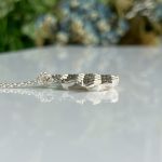 Close-up of a textured silver pendant on a delicate chain laid on a glossy white surface.