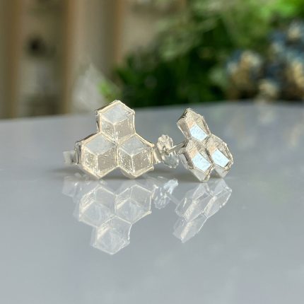 Silver hexagon honeycomb earrings resting on a reflective surface, showing their geometric facets.