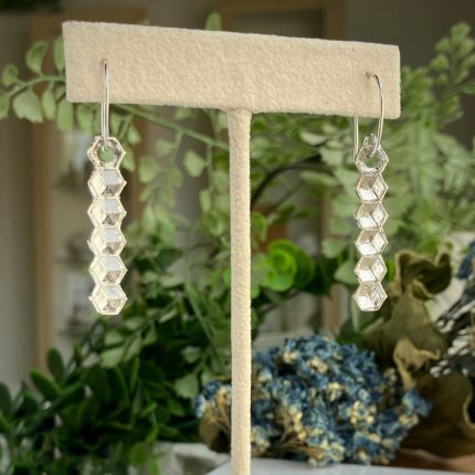 Dangling silver earrings with stacked hexagonal beads displayed on a beige jewelry stand.