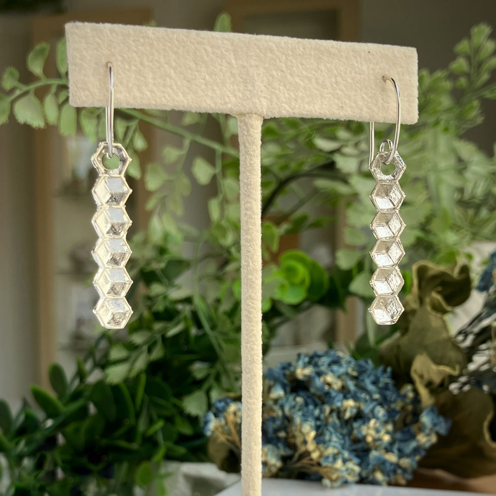 sterling silver honeycomb drop earringsjpeg | Posy Fine Jewellery Toronto Dangling silver earrings with stacked hexagonal beads displayed on a beige jewelry stand.