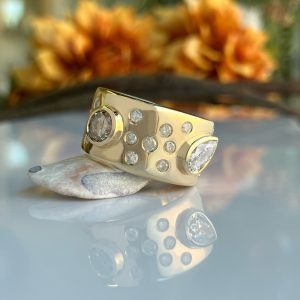 Close-up of a gold bracelet with crystal-studded sections resting on a reflective surface, blurred autumn leaves in the background.