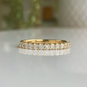 Gold band encrusted with evenly spaced diamonds in a pavé setting on a reflective surface at close range.