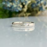Close-up of a hammered silver ring resting on a glossy surface with a blurred outdoor background