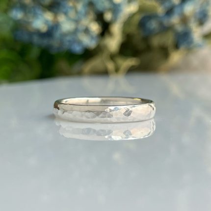 Close-up of a hammered silver ring resting on a glossy surface with a blurred outdoor background