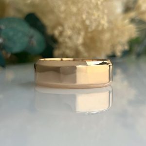 Gold wedding band resting on a reflective surface with a blurred floral background.