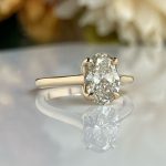 Gold ring with a large oval-cut diamond in a four-prong setting on a reflective surface.