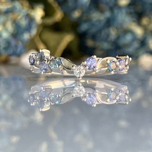 Close-up of a crystal bracelet with clear and lavender stones on a reflective surface, background blurred.