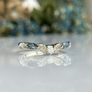 Silver ring with a central diamond flanked by blue gemstones, resting on a reflective surface.