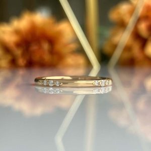 Gold ring with small diamonds along the band, reflected on a glossy surface.