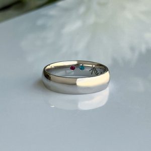 Two-tone band ring with pink and blue gemstones resting on a reflective surface.