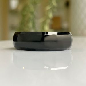 Close-up of a glossy black circular wearable device lying flat on a white reflective surface.