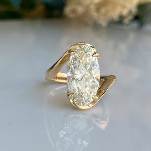 Gold wrap ring with a large oval-cut diamond held by prongs in a bypass design.