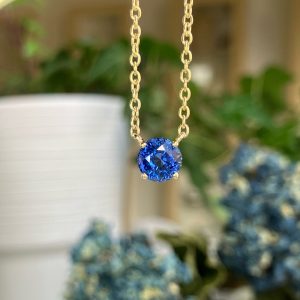 Gold chain necklace with a round deep-blue gemstone pendant, suspended against a blurred background.
