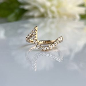 Crescent-shaped gold ring studded with diamonds on a reflective surface.