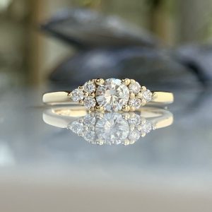 Close-up of a diamond engagement ring with a halo of smaller stones on a reflective surface.
