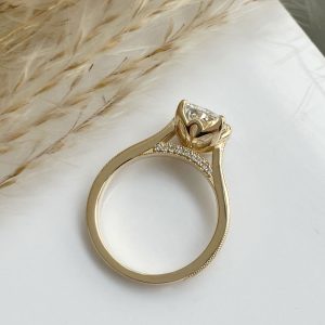 Yellow gold engagement ring with a solitaire diamond and pavé diamonds along the band on a white surface.