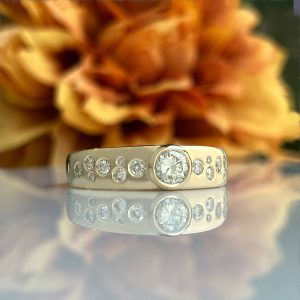 Close-up of a silver diamond ring with a large central gem and many small stones, reflected on a glossy surface.