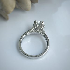 Close-up of a silver engagement ring with an empty center setting and intricate filigree on the band.