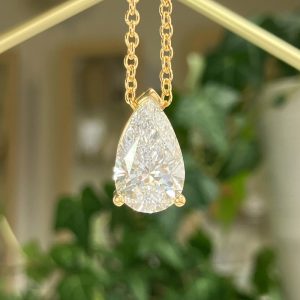 Teardrop/pear-cut diamond pendant on a gold chain against a soft blurred background.