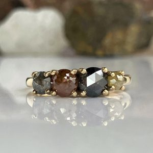 Gold ring with a row of five faceted gemstones in gray, brown, black, and olive tones set in prongs.