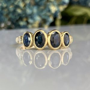 Row of gold rings with deep blue gemstones, arranged on a reflective surface