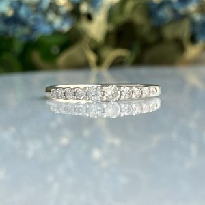 Close-up of a diamond-studded ring resting on a reflective surface with a blurred outdoor background.