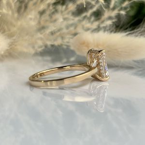 Gold engagement ring with a rectangular-cut diamond in a raised prong setting and small side diamonds on a reflective surface