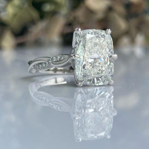 Diamond ring with a large cushion-cut diamond held by four prongs, reflected on a glossy surface
