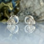 Pair of silver flower-shaped stud earrings with petal detailing resting on a reflective surface.