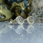 Silver round stud earrings with ornate scalloped bezels, reflection visible on a glossy surface.