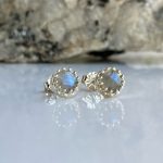 Pair of silver stud earrings with round blue iridescent stones and a beaded bezel on a reflective surface.