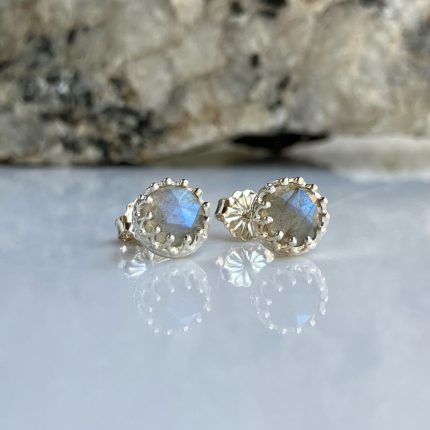 Pair of silver stud earrings with round blue iridescent stones and a beaded bezel on a reflective surface.
