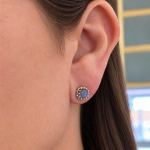 Close-up of a woman's ear wearing a round blue gemstone stud with a silver beaded halo.