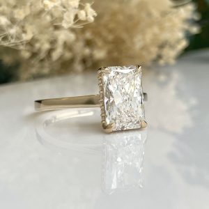 Emerald-cut diamond engagement ring with a gold band on a reflective surface.