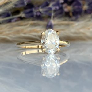 Gold ring with an oval-cut diamond centerpiece, reflected on a glossy surface.