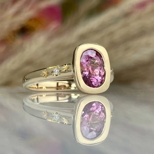 Two-tone ring: pink oval gemstone set in a gold bezel with small diamonds along the band and star engravings on the side.
