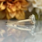 Close-up of a silver engagement ring with a solitaire diamond resting on a reflective surface