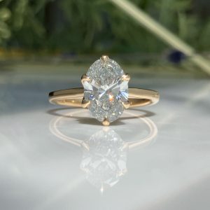 Rose gold solitaire engagement ring with a large oval diamond in a four-prong setting, on a glossy reflective surface.