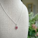Silver chain necklace with an oval pink gemstone pendant set in a silver bezel, displayed on a beige fabric mannequin form.